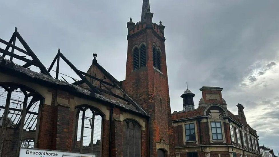 A still of a burnt-out church, as the remaining walls and window frames are black.