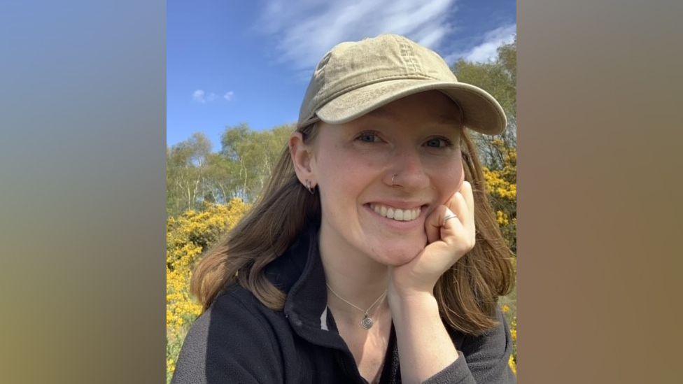 Photograph of Lily Sparrow. She has shoulder length brown hair and is wearing a baseball cap