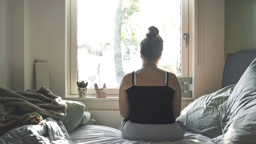 A woman looks out of the window sitting on her bed