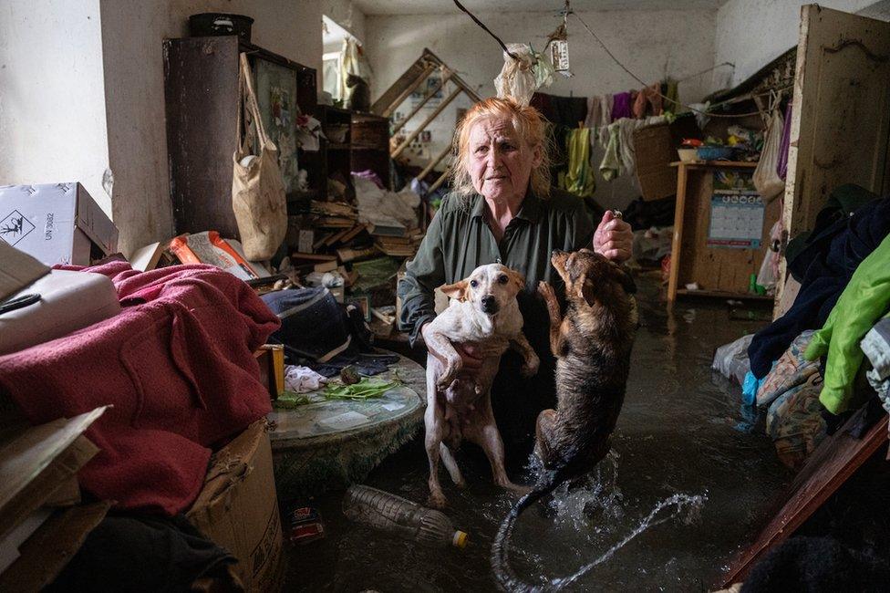 An elderly woman carries her pets out from her flooded house