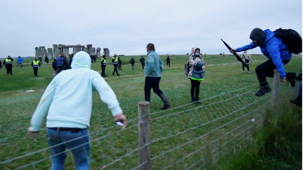 People climb over a fence to get into Stonehenge ancient stone circle during the Summer Solstice celebrations