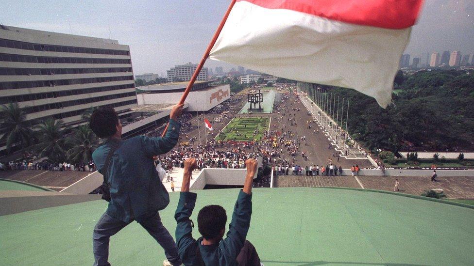 Students stand on the roof of the parliament building waving the Indonesian flag as they demand the resignation of president Suharto May 20, 1998 in Jakarta, Indonesia.