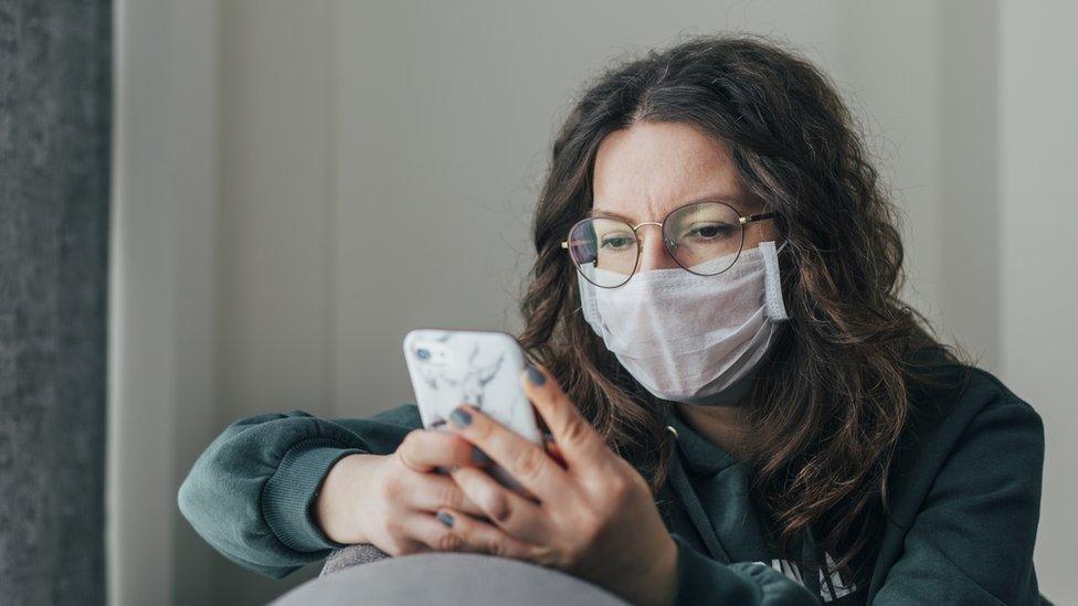 Woman holding phone wearing mask