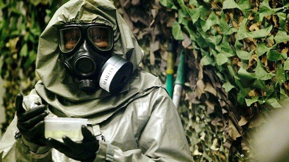 An instructor at the Fort Leonard Wood Chemical School, who is designated as an agent handler, carries the VX nerve agent to contaminate a jeep in one of the eight chambers used for training chemical defense 18 April 2003 at Fort Leonard Wood, Missouri.