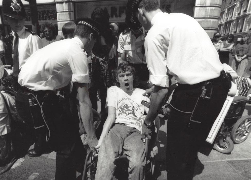 A wheelchair user being lifted up by police