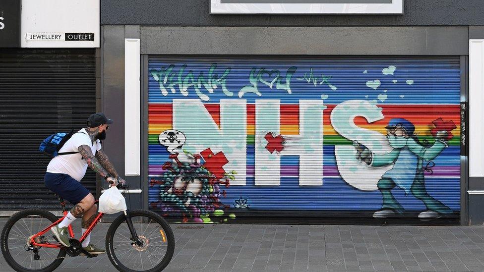 Man wearing a mask cycling past an NHS art graffiti mural in Hull