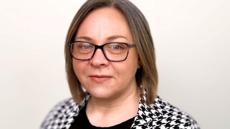 Woman - Morven Brooks from Voluntary Action Orkney - looking at camera, wearing glasses and a black and white checked top