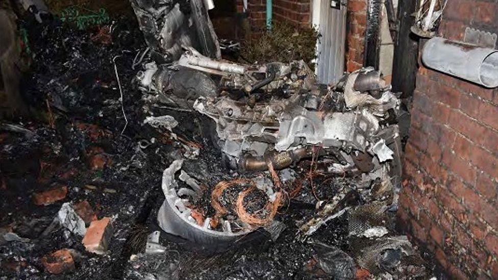 Gnarled black twisted wreckage of an unrecognisable car.