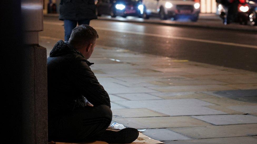 A homeless person on the street as cars pass by