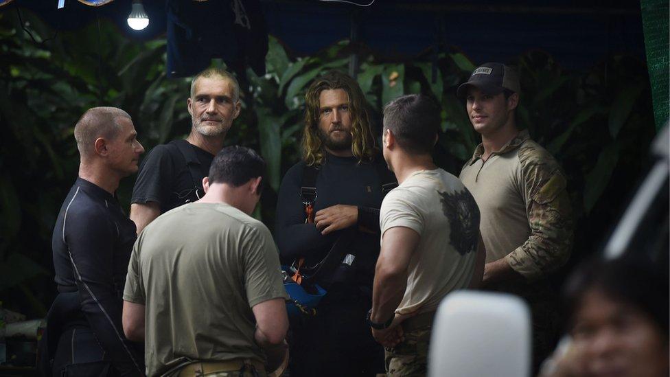 A group of foreign divers and US soldiers, wearing light colored shirts, gather at the Tham Luang cave area as rescue operations continue for the 12 boys and their coach trapped at the cave in Khun Nam Nang Non Forest Park in the Mae Sai district of Chiang Rai province on July 6, 2018