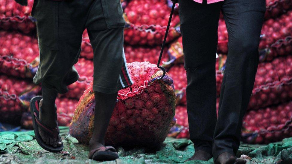 Indian labourers unload sacks of onions from a truck at Mundera wholesale market in Allahabad