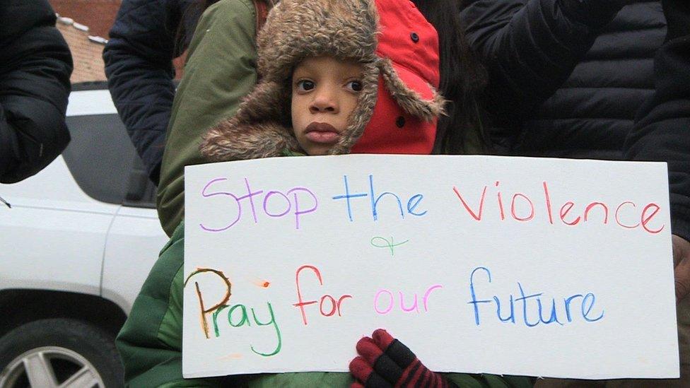 Child at a demo with a banner that says "Stop The Violence"