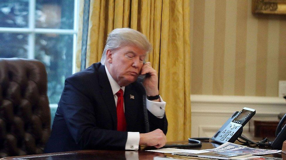 President Donald Trump is seen through a window speaking on the phone with King of Saudi Arabia