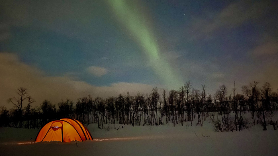 Tent glowing in the snow with the Northern Lights on display