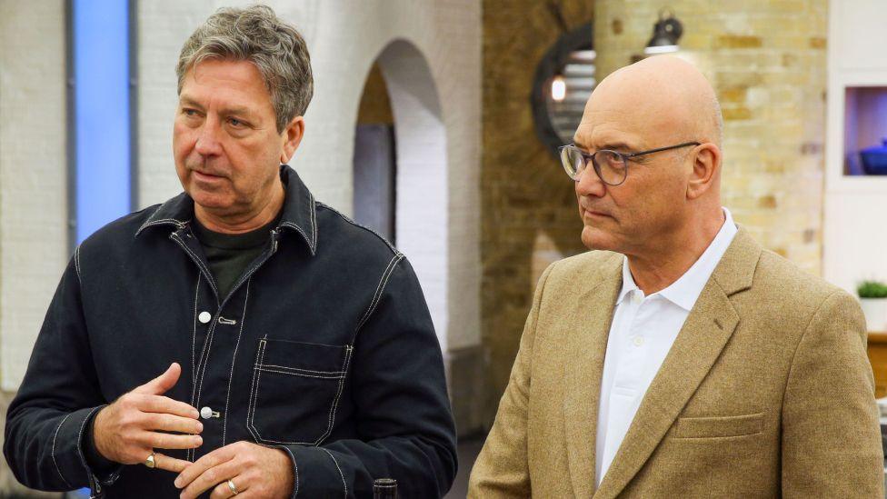John Torode and Gregg Wallace pictured on MasterChef, looking towards a contestant, with the MasterChef studio seen in the background