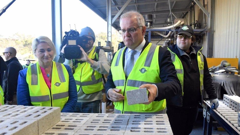 Scott Morrison wearing a high-viz vest holding a brick.