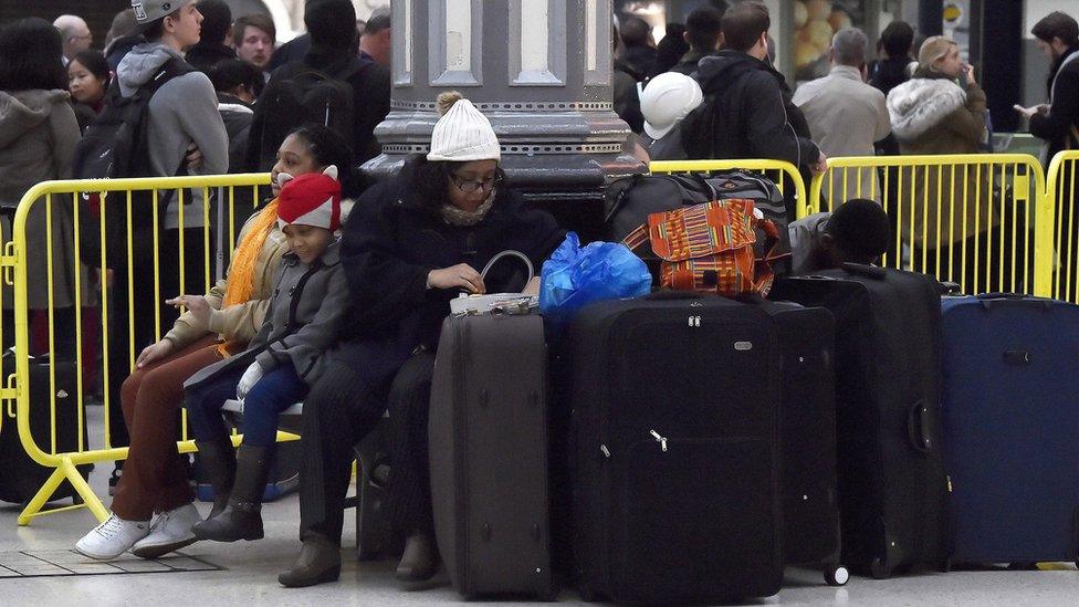 woman and family surrounded by luggage wait in station