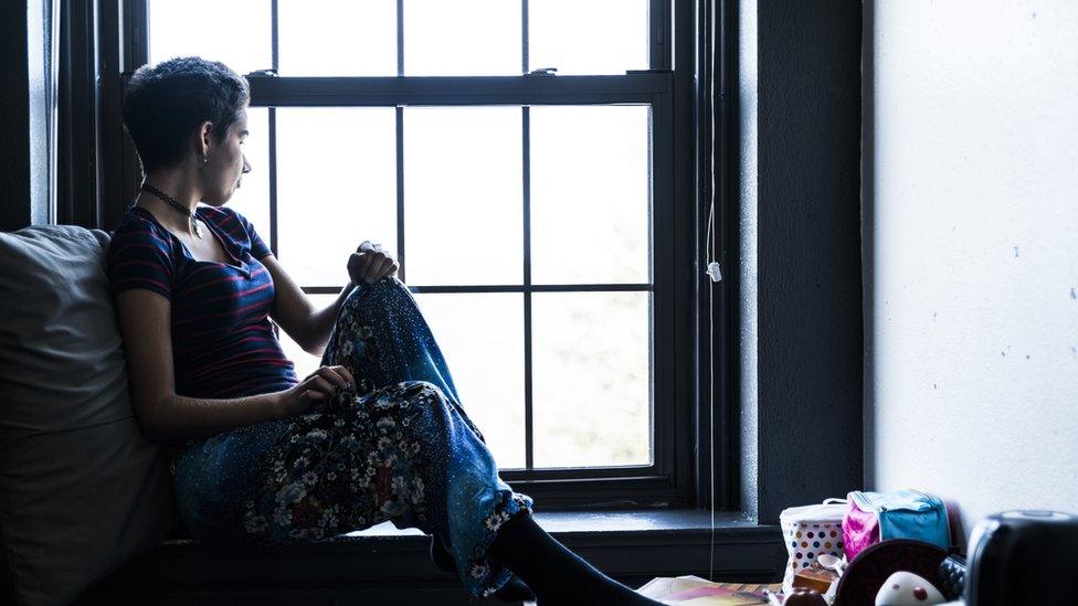 A young woman looks out from a window in a hotel room