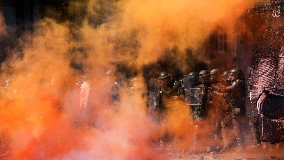 Riot police stand amid tear gas and smoke from a burning barricade during a protest against Chile's government in Concepcion on 12 November, 2019