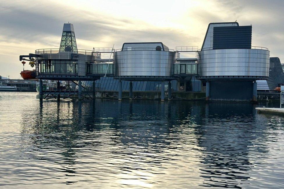 A metallic looking museum reflected on a lake