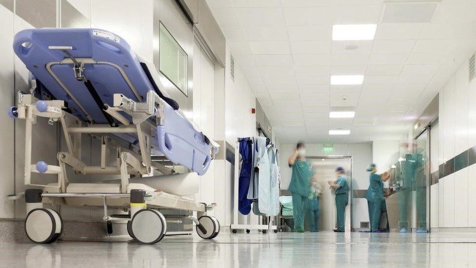 An image of a hospital corridor with a stretcher at the left, and staff wearing green surgical uniforms