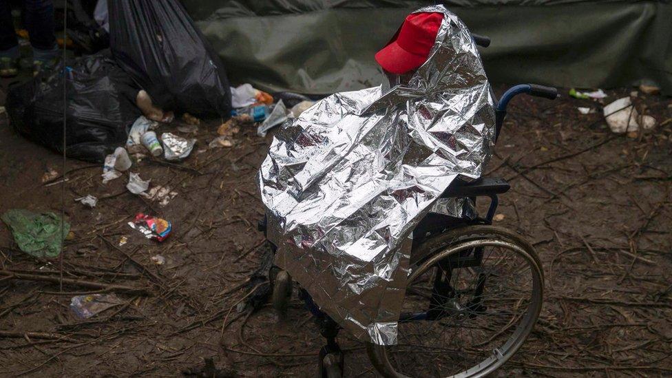 A migrant on a wheelchair protects himself from the rain near the border crossing with Croatia, near the village of Berkasovo, Serbia October 19, 2015.