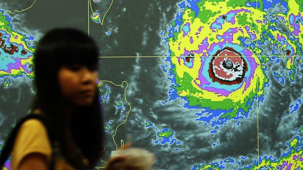 A Taiwanese walks past a video screen with the graph of Typhoon Nepartak heading towards Taiwan