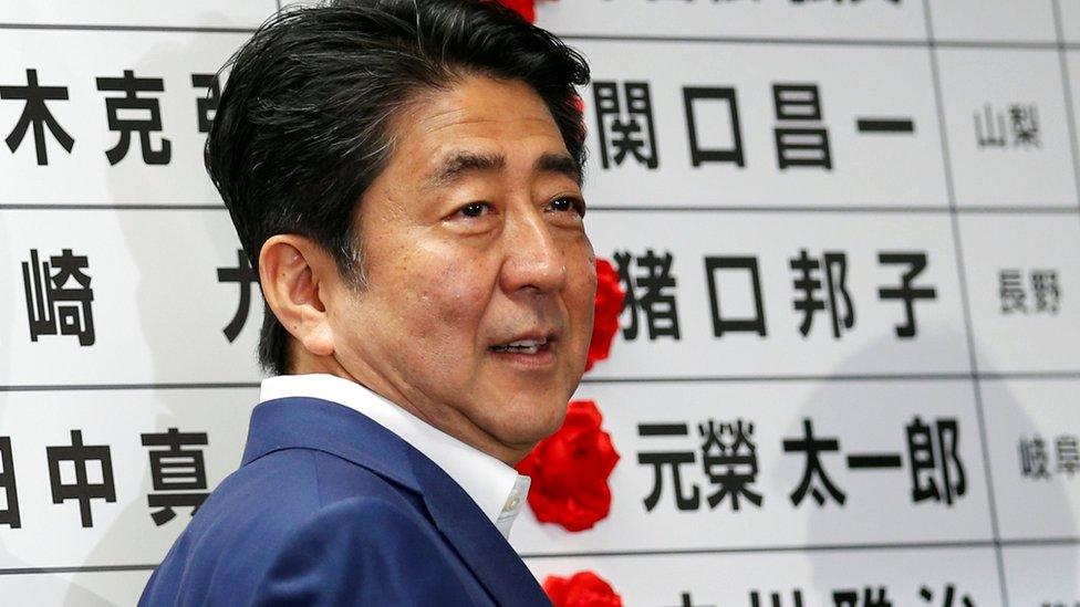 Japan's Prime Minister Shinzo Abe smiles as he puts a rosette on the name of a candidate who is expected to win the upper house election at the LDP headquarters in Tokyo, Japan on 10 July