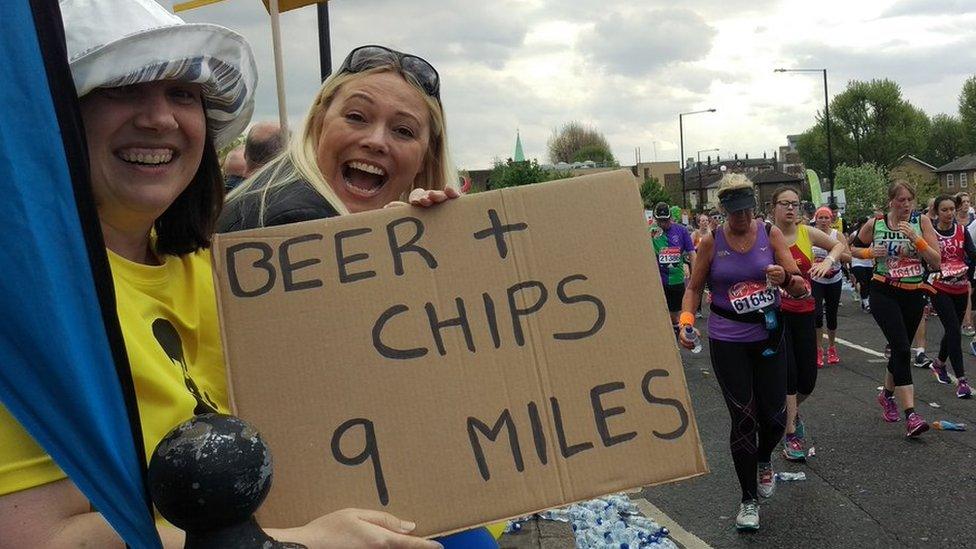 Two women stand with a cardboard sign saying 'Beer and chips nine miles'