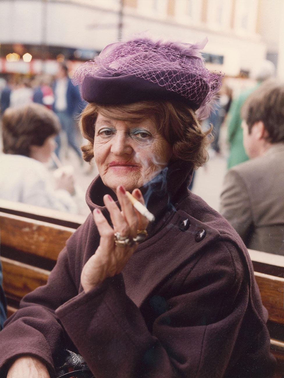 A woman sits on a street bench smoking a cigarette