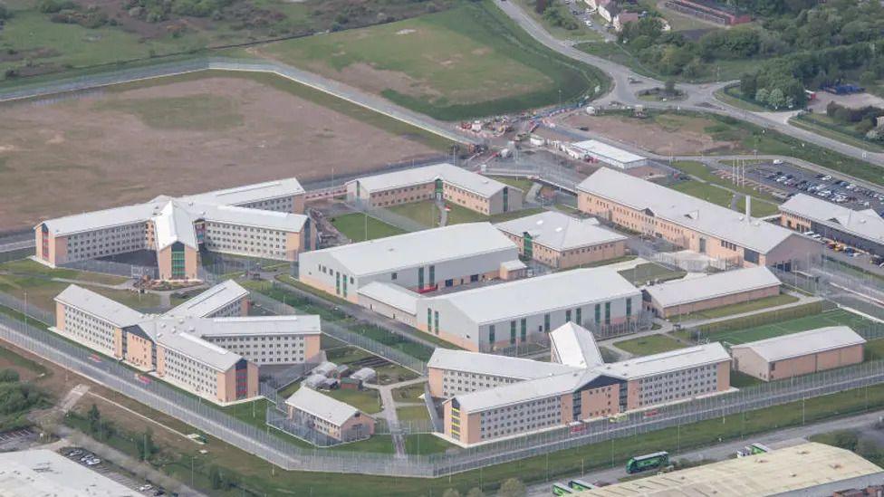 An aerial shot of HMP Berwyn showing a square site with various buildings running alongside the edges and a larger building in the middle. Square patches of grass can be seen between the buildings.