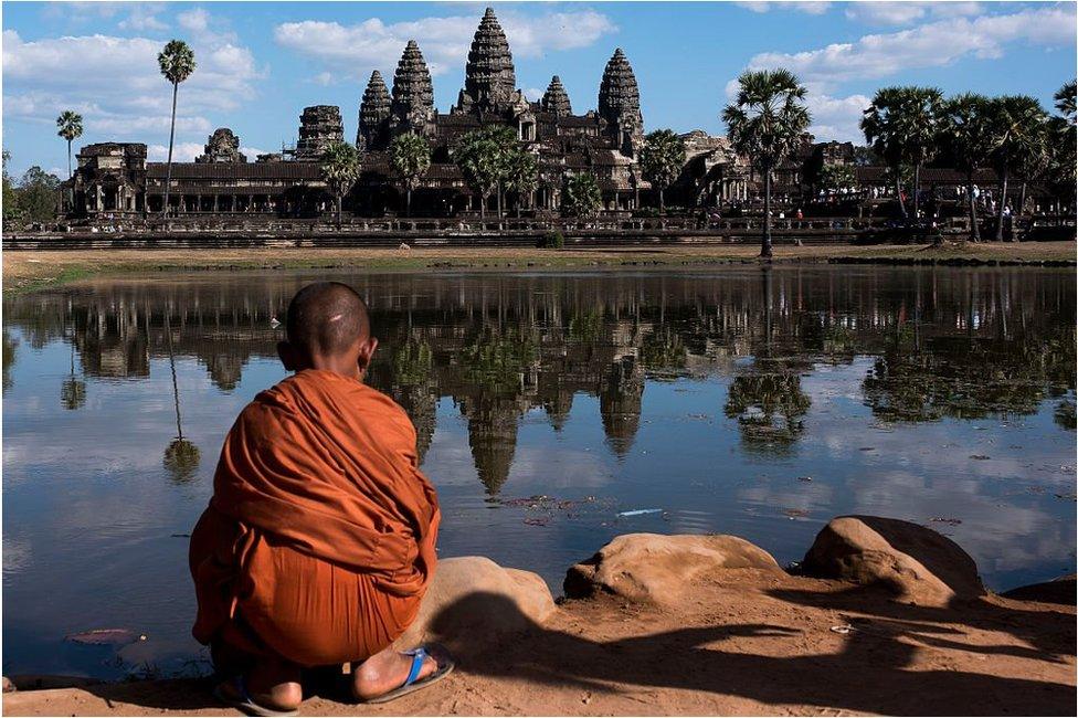 A young monk sits in front of a lack in front of the Angkor Wat temple on 1 January 2016, near Siem Riep, Cambodia.