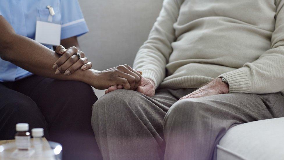 A nurse holding an older man's hand