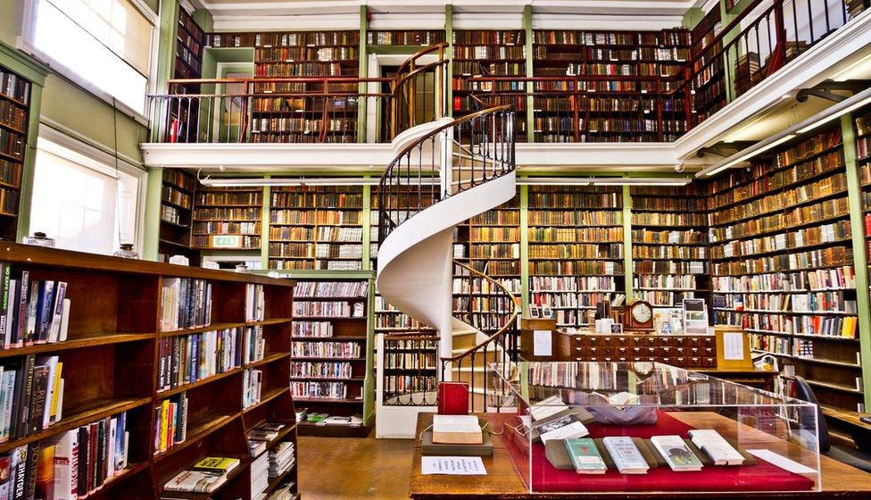 Inside a room at the Leeds Library with bookshelves from top to bottom of the two-storey room and a spiral staircase leading to the second level.