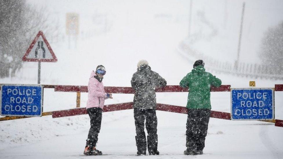 Members of the public stand near a closed road in the snow