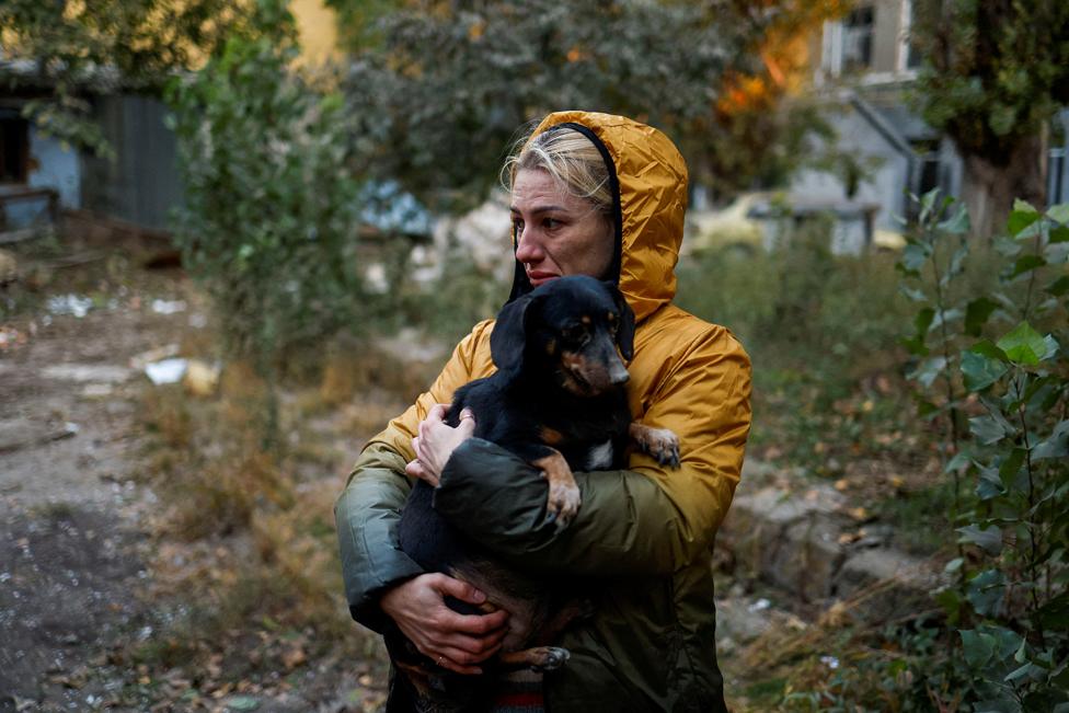 A woman carries a dog at a site of a residential building heavily damaged by a Russian missile strike in Mykolaiv, Ukraine, 18 October 2022.