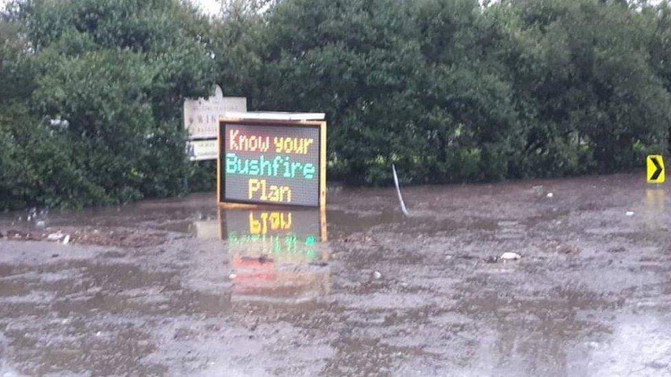 Flood waters lap a bushfire warning road sign