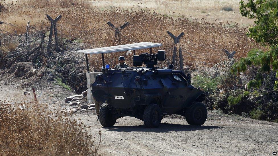 A Turkish soldier stands next to an armoured personnel carrier securing a road near the border with Syria, as seen from the outskirts of the village of Seve, east of the town of Kilis, in south-east Turkey, Friday, July 24, 2015.