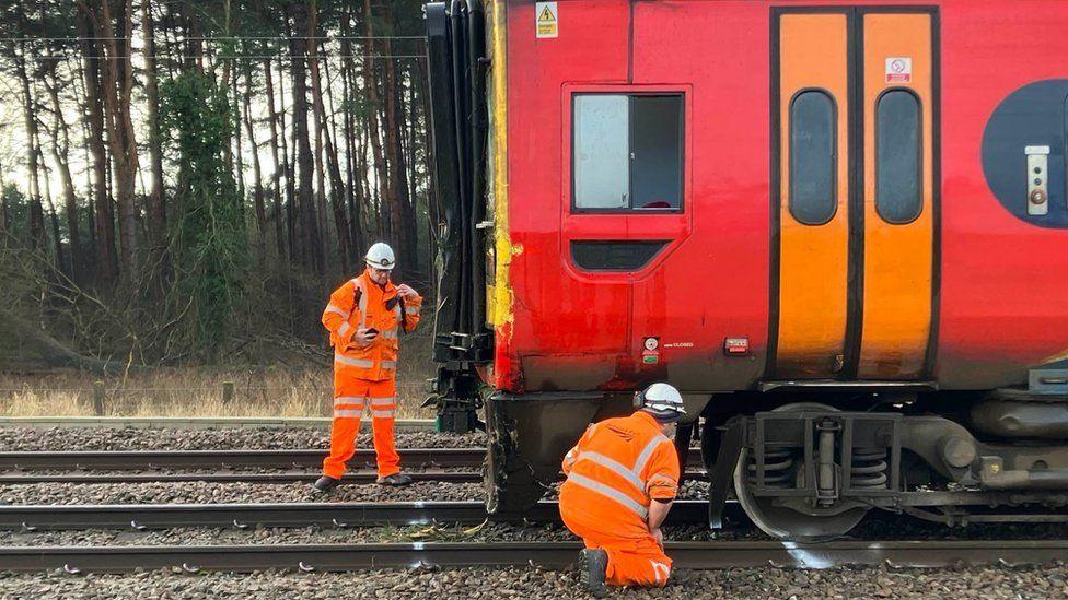 Two engineers inspecting the front of the train, which has come off its tracks.