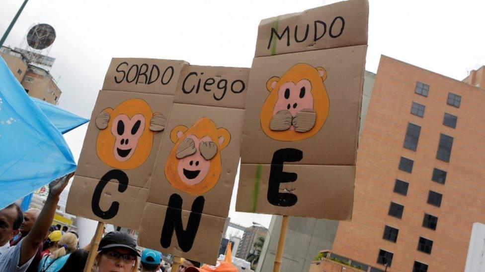 Opposition supporters hold placards during a rally to demand a referendum to remove President Nicolas Maduro in Caracas, Venezuela, May 14, 2016. The placards (L-R) read "Deaf", "Blind" and "Dumb". "CNE" on the placards refers to the National Electoral Council. REUTERS