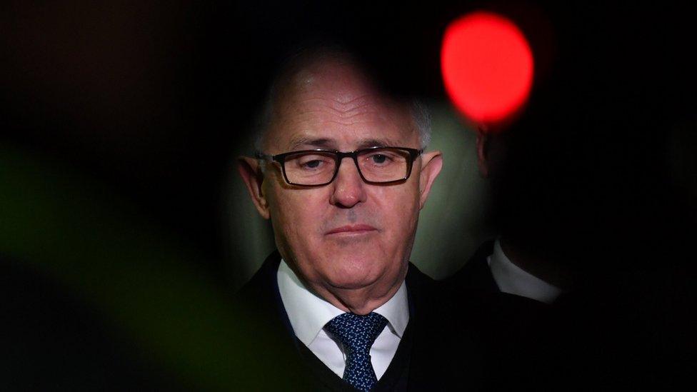 A close-up shot of Prime Minister Malcolm Turnbull framed by shadow next to a red light