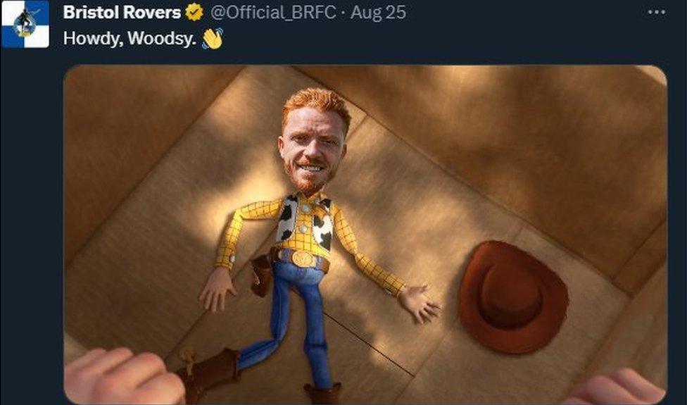 A screengrab of Bristol Rovers' tweet announcing the signing of Ryan Woods. The text above the image says "Howdy, Woodsy" and has a waving hand emoji after it. The image underneath is taken from the Toy Story films and shows the cowboy character Woody lying in a cardboard box with his cowboy hat next to him. But the player Ryan Woods face has been superimposed where Woody's face would be.