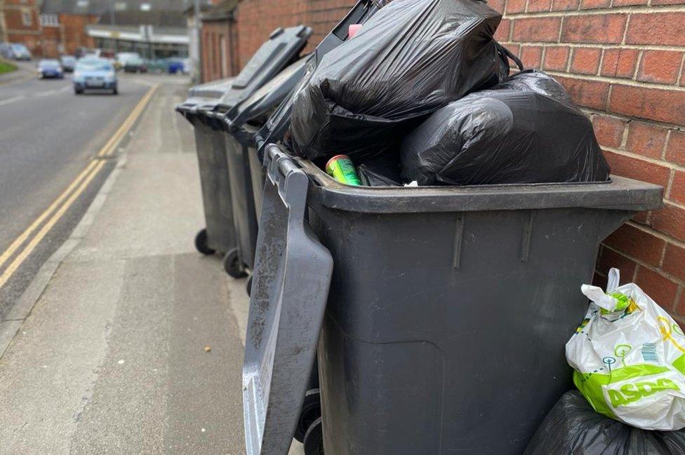 An open black bin with rubbish piled up inside