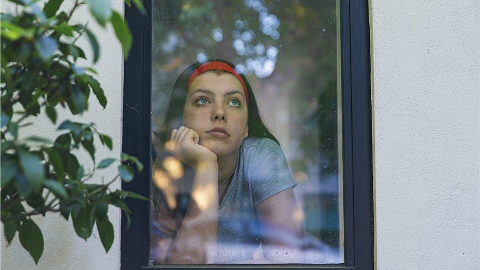 teenage girl looks out of a window