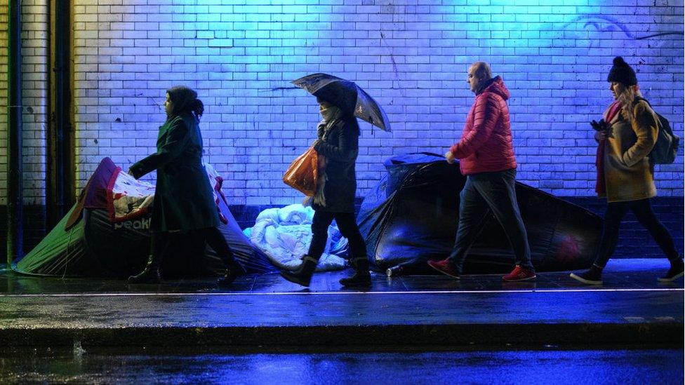 Commuters walk past homeless people