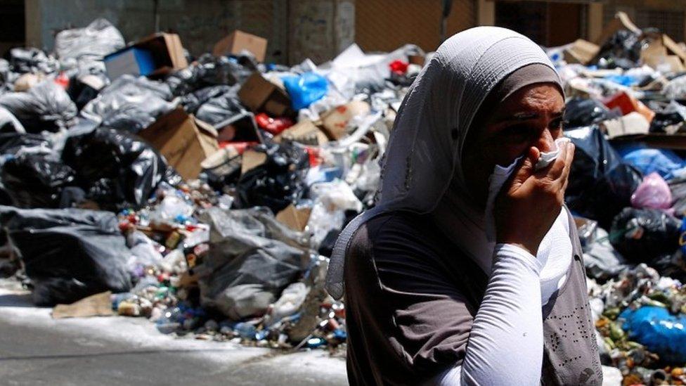 A Lebanese woman covers her nose from the smell as she walks on a street partly blocked by piles of garbage in Beirut 17 July 2015)