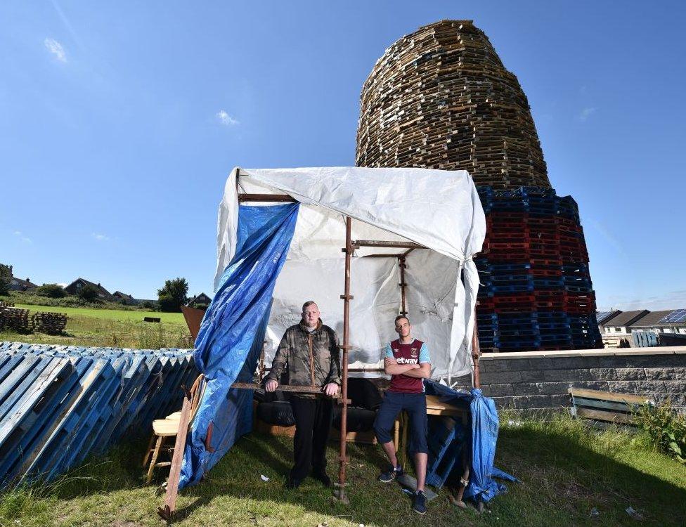 Brothers Mark (L) and Hayden (R) watch over the nearly completed bonfire on the Ballyduff estate from their makeshift shelter on July 10, 2017 in Newtownabbey, Northern Ireland.