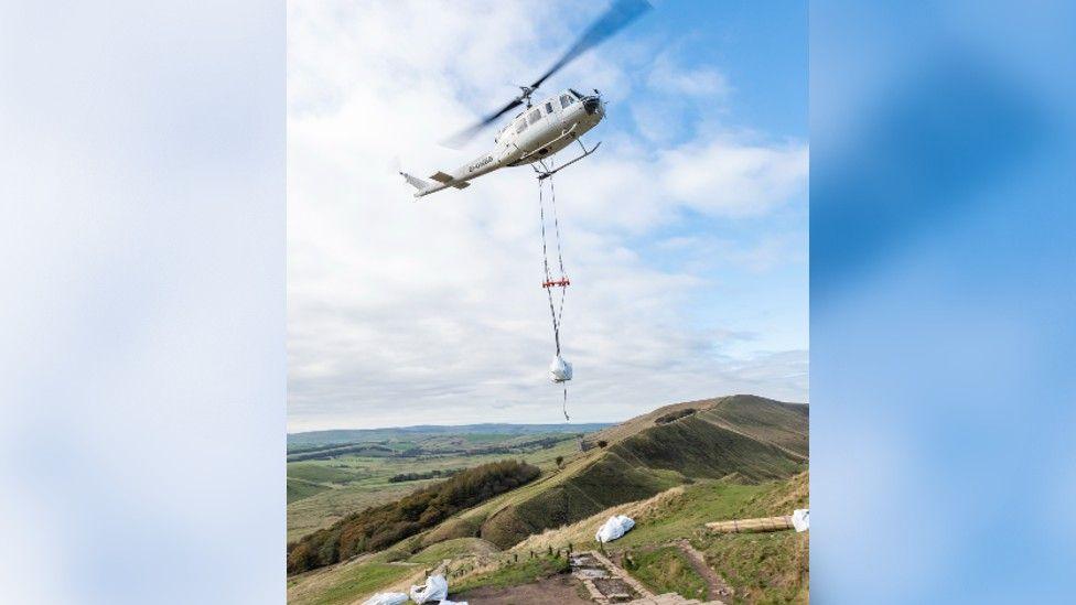 A helicopter airlifting a bag of materials to the top of a hill in the Peak District in Derbyshire 