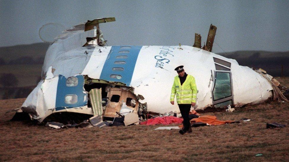 A lone police officer walks past the wreckage of Flight Pan Am 103, which came down in a field over Lockerbie