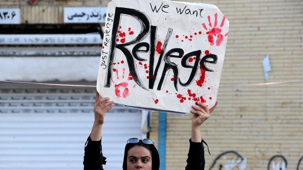 An Iranian mourner holds a placard in funeral procession saying 'We want revenge'